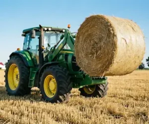 Green tractor lifting a large round hay bale in field.